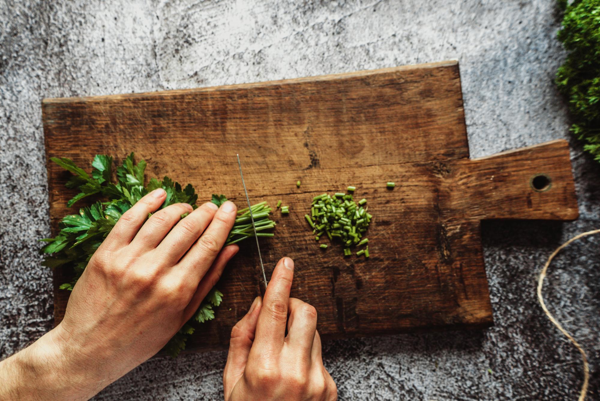 Hands cutting herbs over a wooden board